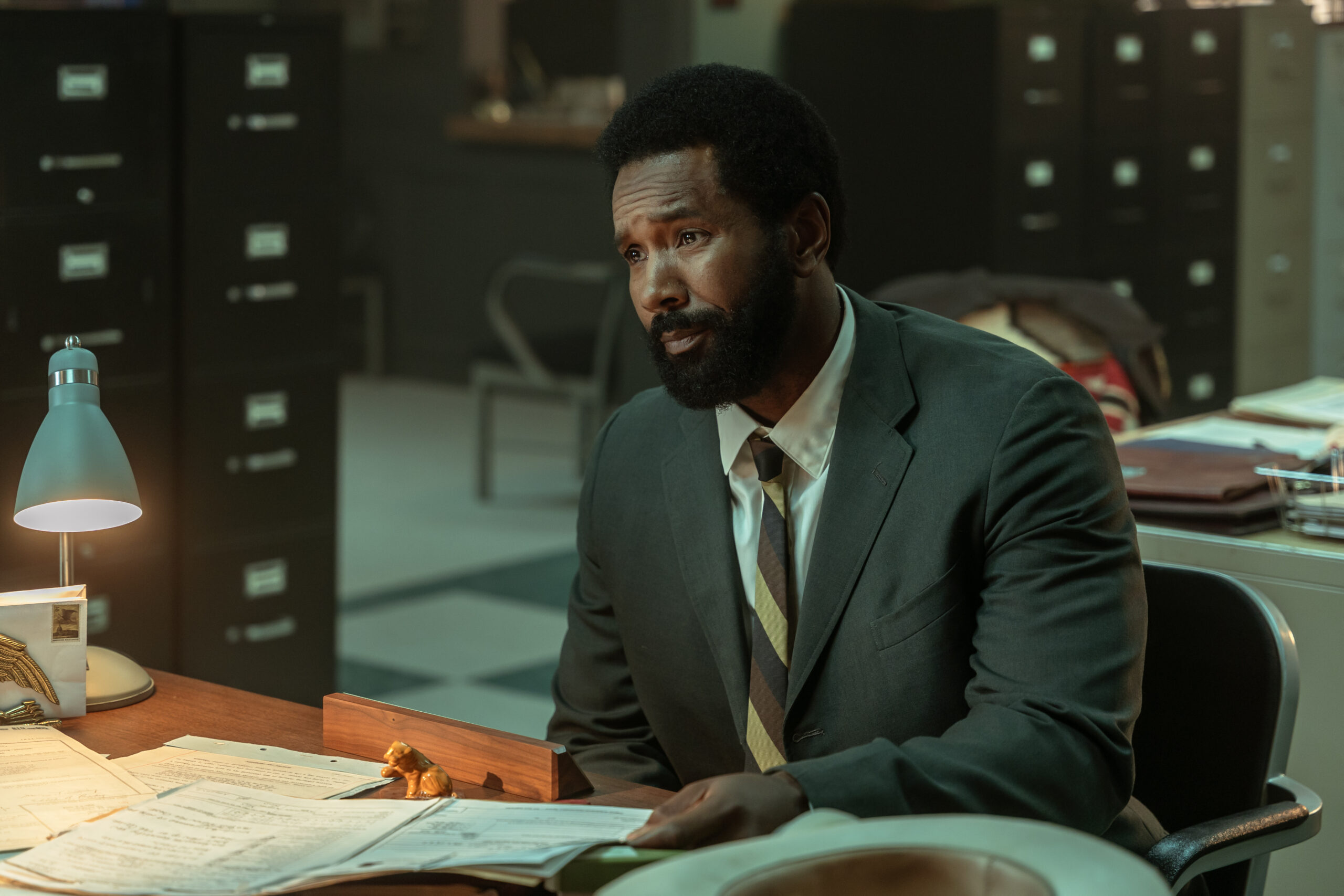 Dark Winds Season 2 Episode 5 - Tank Jones | Tell-Tale TV Still from Dark Winds Season 2 Episode 5 of Tank Jones as Deloyd Webster sitting at a desk wearing a suit and tie