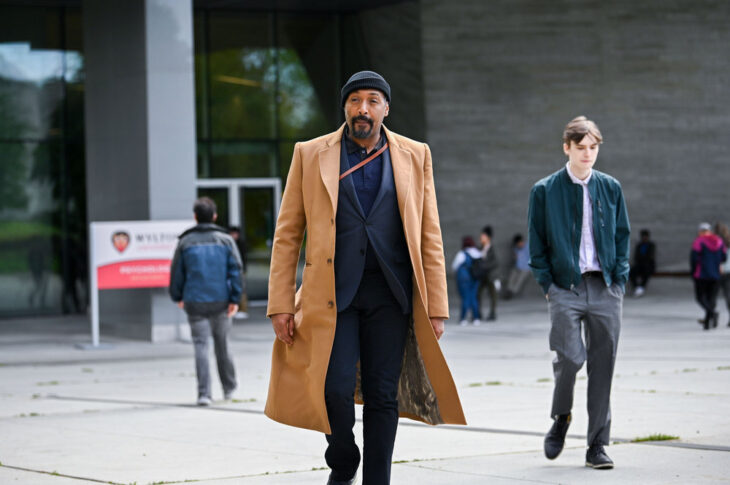 Still from The Irrational Season 1 Episode 1 of Martin as Alec Mercer walking outside in a black suit with a tan trench coat and black beanie