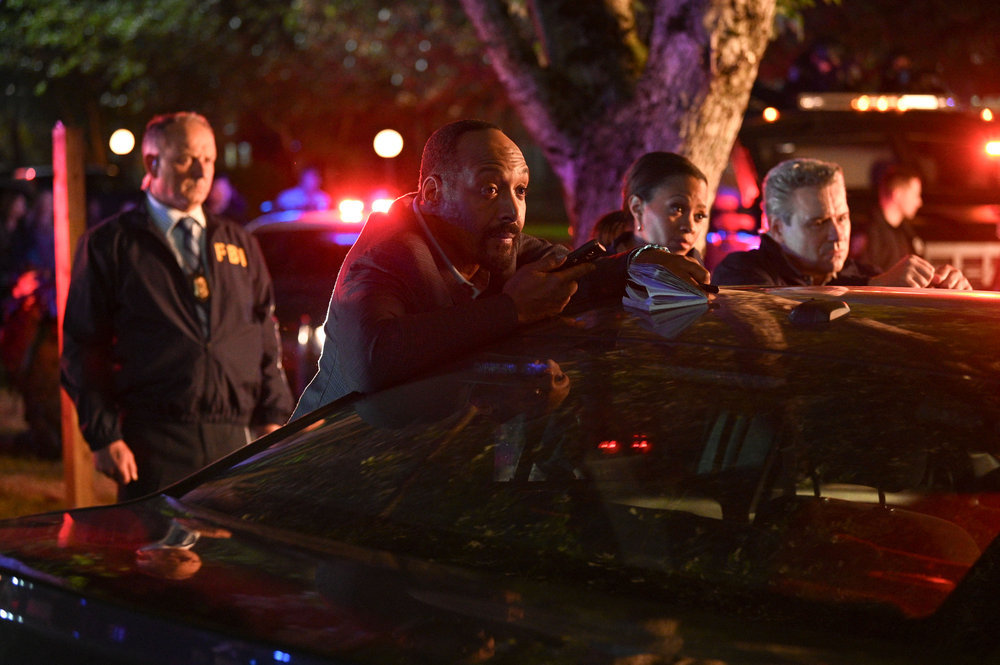 Still from The Irrational Season 1 Episode 1 of Jesse L. Martin as Alec Mercer, Maahra Hill as Marisa standing behind a car at a night time crime scene