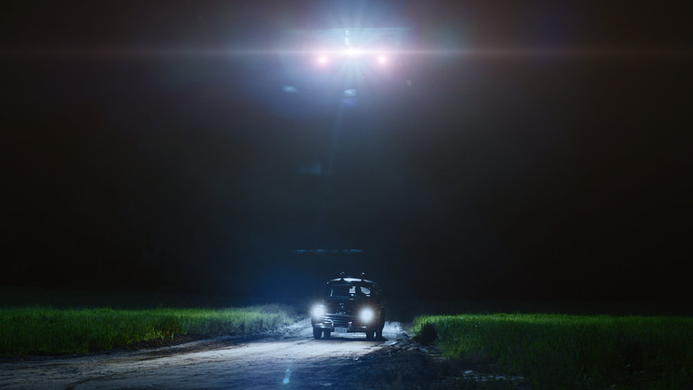 Still from Quantum Leap Season 2 Episode 3 of a Sheriff's Car driving on a dark road with lights from an aircraft above