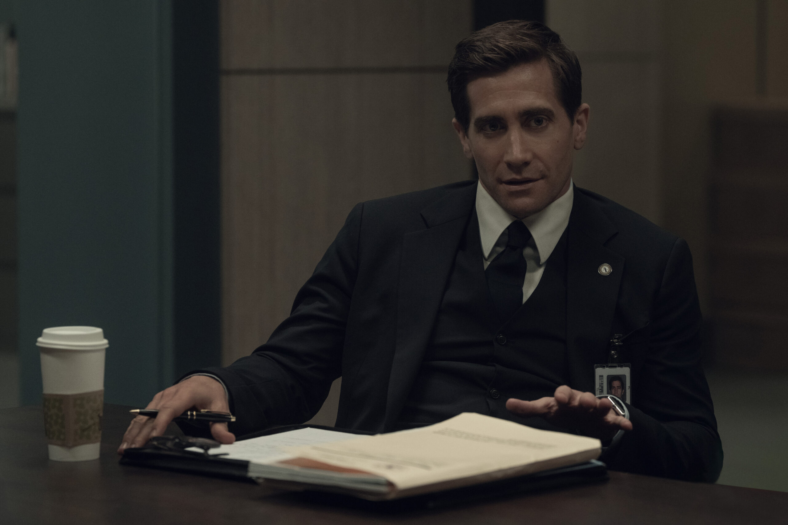 Jake Gyllenhaal sitting at a desk with a notebook opened.
