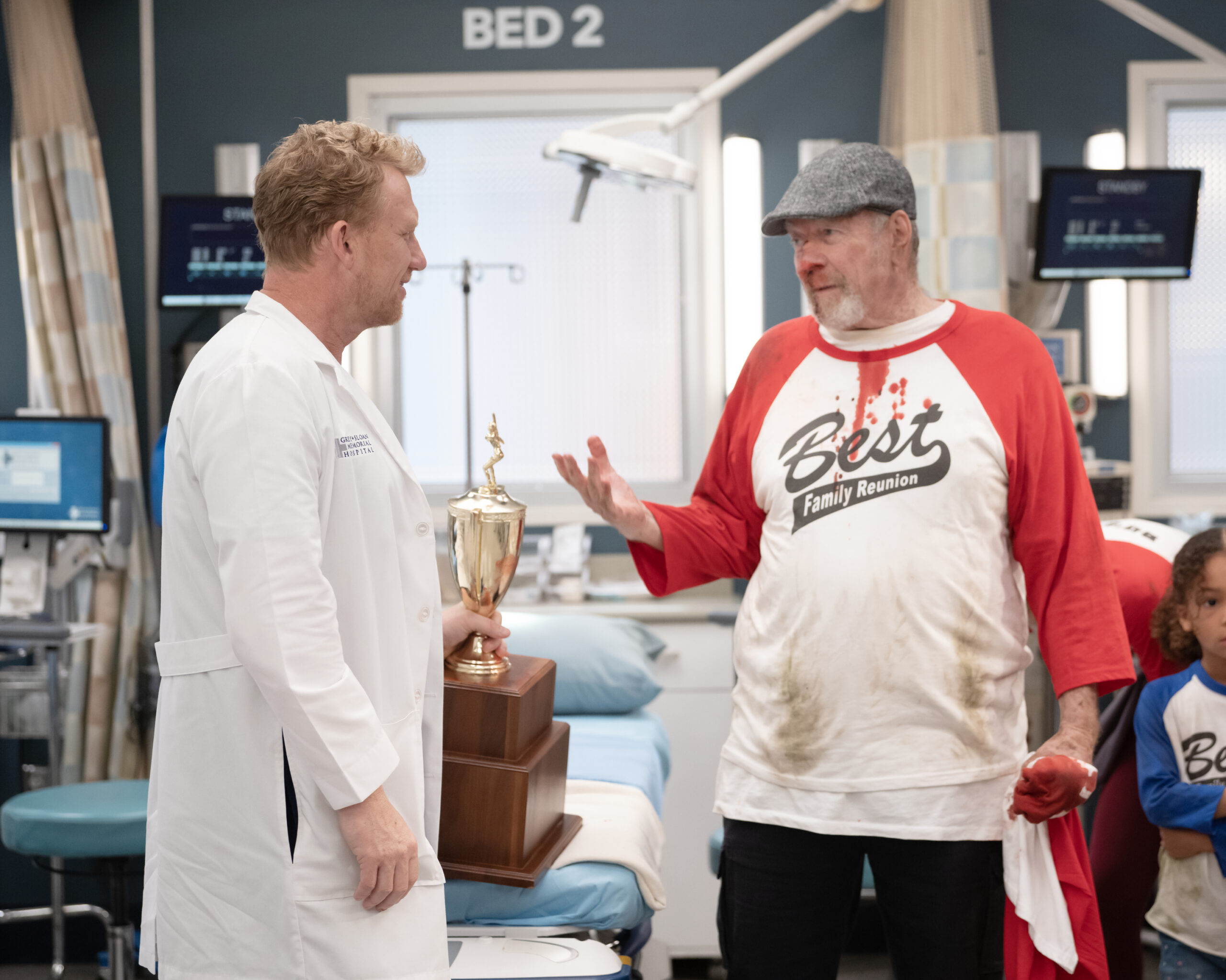 Owen talks to a patient, baseball coach, and holds a trophy on Grey's Anatomy Season 20 Episode 2, "Keep the Family Close."