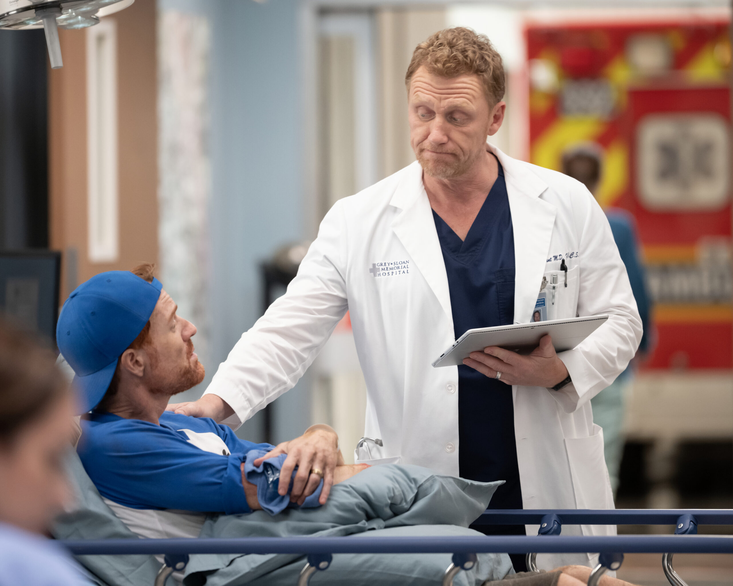 Owen talks to a patient, puts his hand on his shoulder, holds a tablet. KEVIN MCKIDD as Owen Hunt on Grey's Anatomy Season 20 Episode 2, "Keep the Family Close."