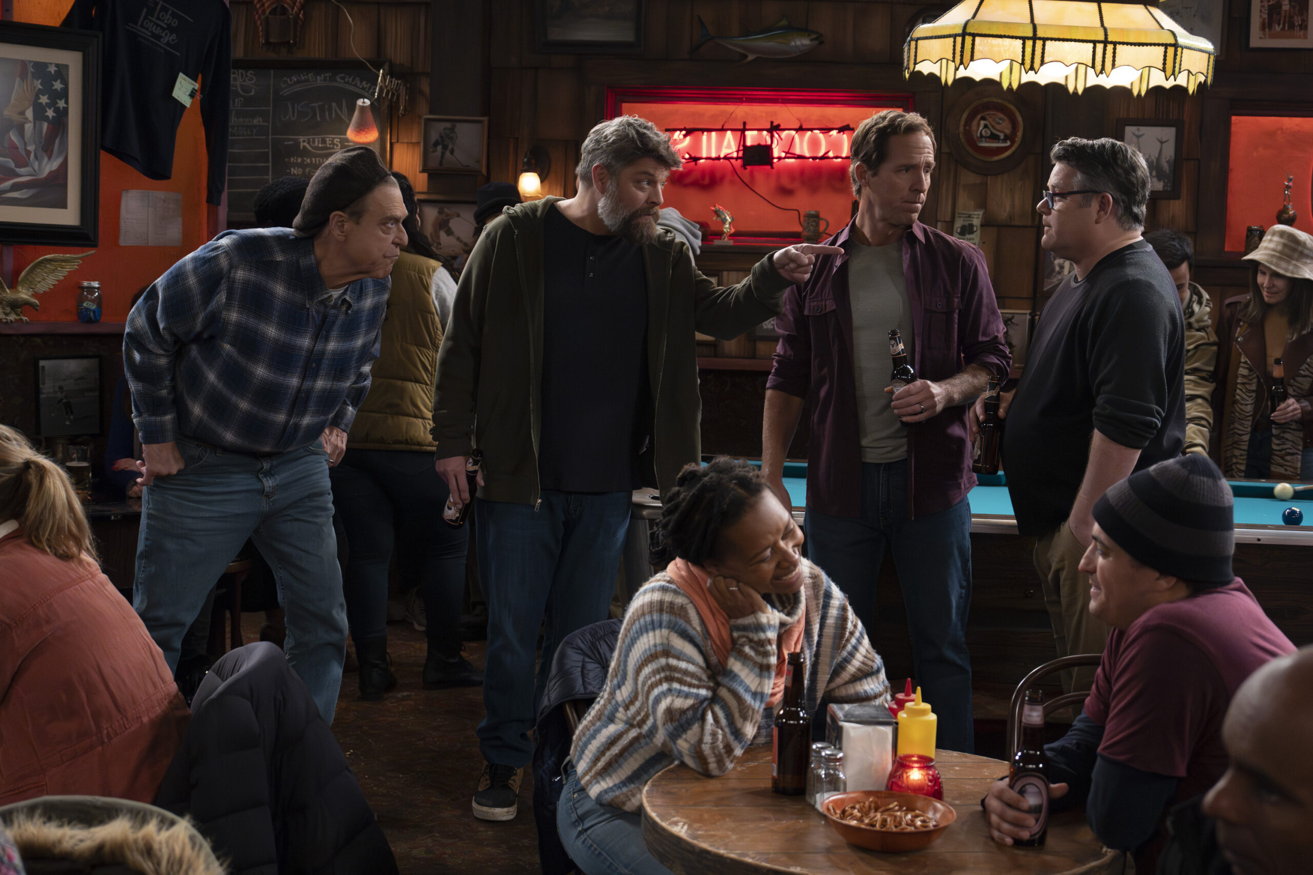 The Conners Season 6 Episode 6 - JOHN GOODMAN, JAY R. FERGUSON, NAT FAXON, SEAN ASTIN hang out in a group at a bar.