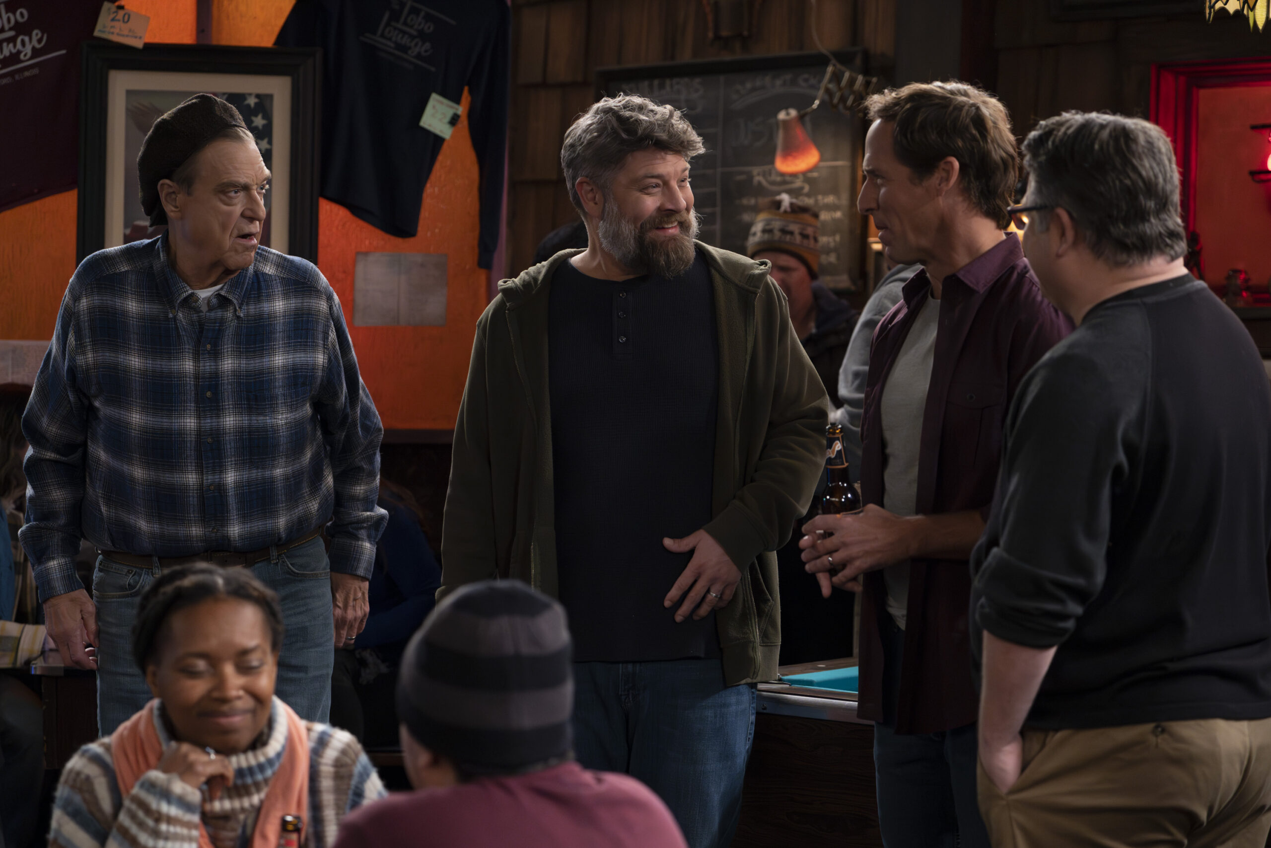 JOHN GOODMAN, JAY R. FERGUSON, NAT FAXON | Tell-Tale TV The Conners Season 6 Episode 6 - JOHN GOODMAN, JAY R. FERGUSON, NAT FAXON hanging out in a group at a bar.