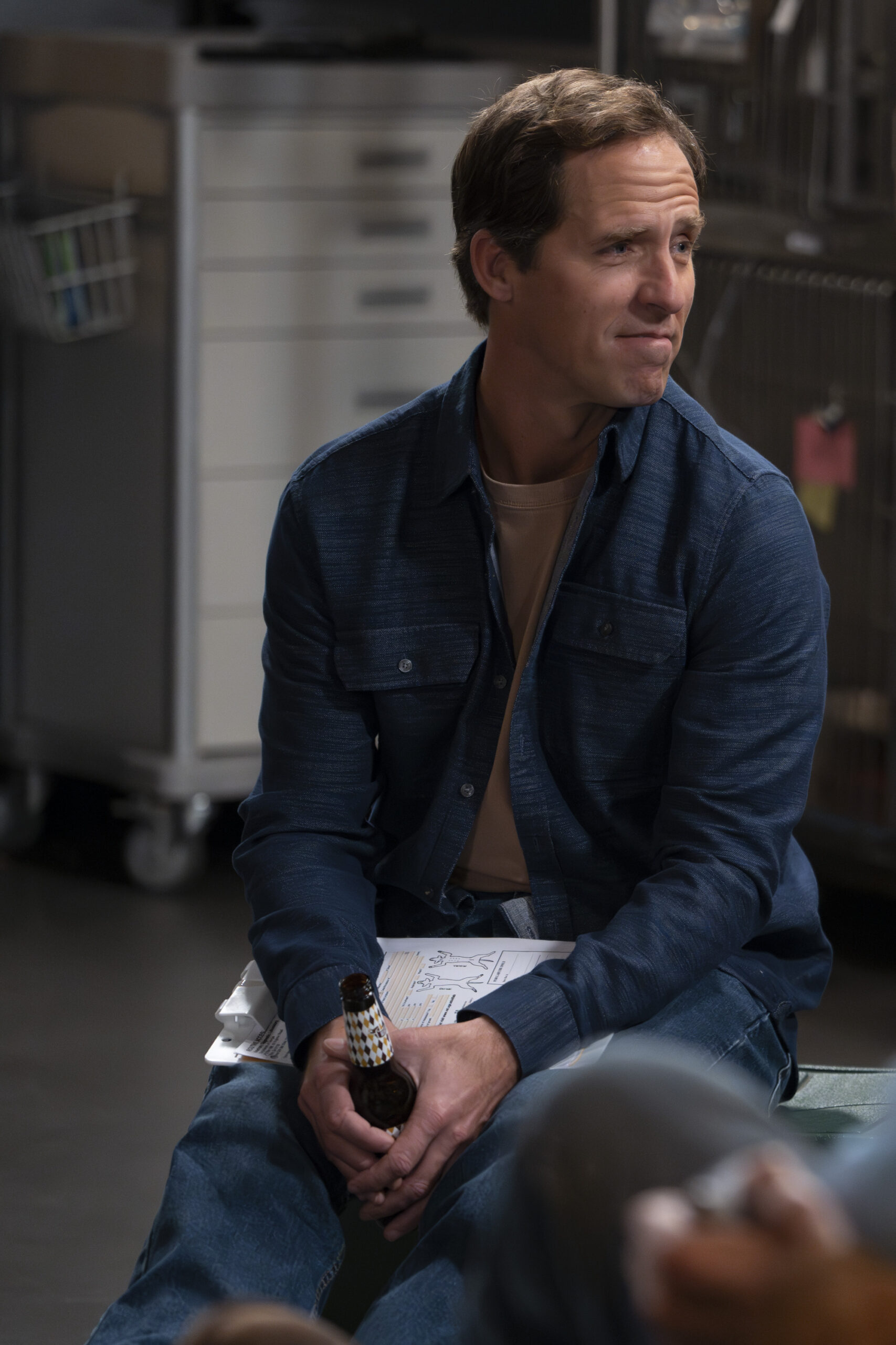 The Conners Season 6 Episode 6 - NAT FAXON sitting in the garage of the Conner family home.