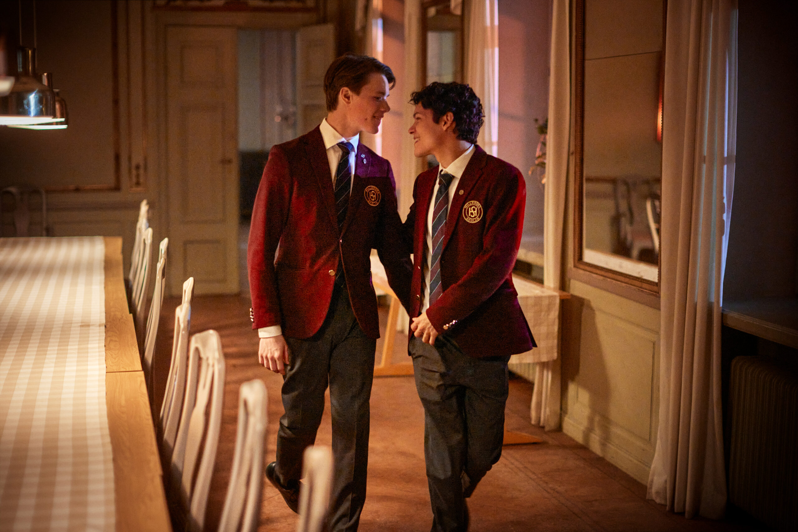 Young Royals S3 | Tell-Tale TV Young Royals Season 3, Edvin Ryding and Omar Rudberg as Wilhelm and Simon walking in the dining hall at school.