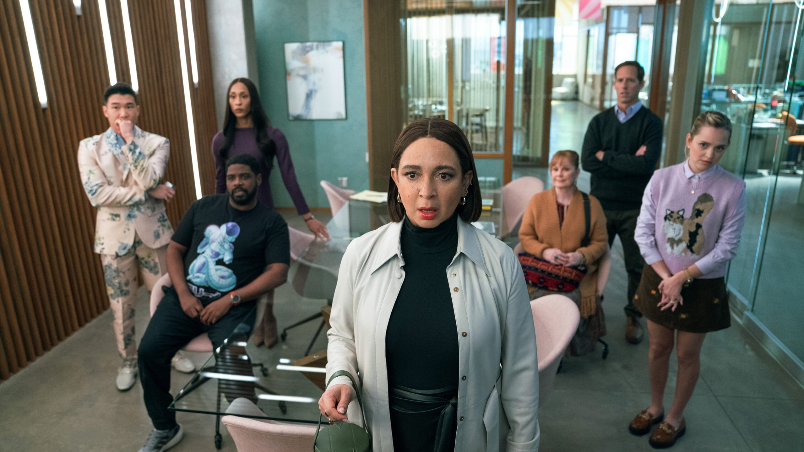 Still from Loot Season 2 Episode 1 of Joel Kim Booster, Ron Funches, Michaela Jaé Rodriguez, Maya Rudolph, Meagen Fay, Nat Faxon and Stephanie Styles in an office with Rudolph standing in front of the group as they all look at something off camera.