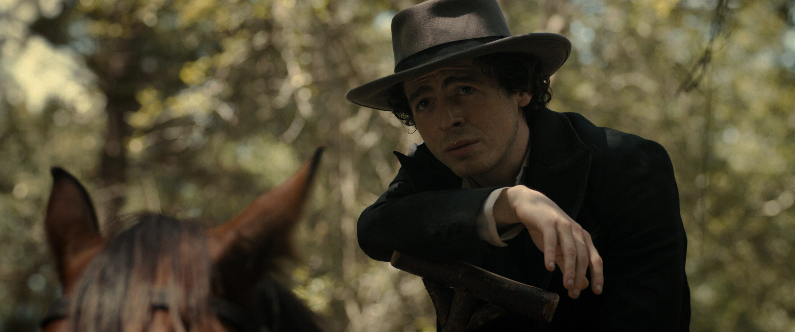 Still from Manhunt Season 1 Episode 3 of Anthony Boyle as John Wilkes Booth wearing a brown hat and dark jacket sitting on a horse