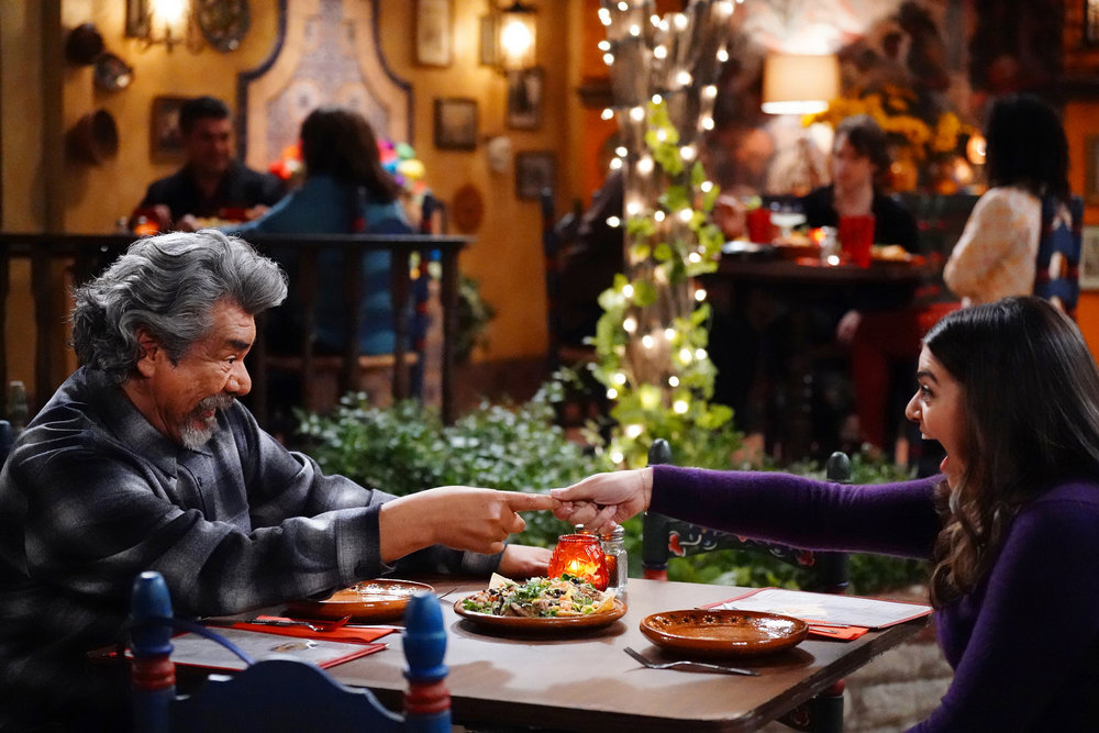 Lopez vs Lopez Season 2 Episode 1: George Lopez sits at a table with Mayan Lopez as they share a meal.