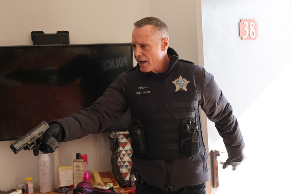 Chicago P.D. Season 11 Episode 7, Jason Beghe as Hank Voight stands in front of the TV in room 38 with his gun extended.