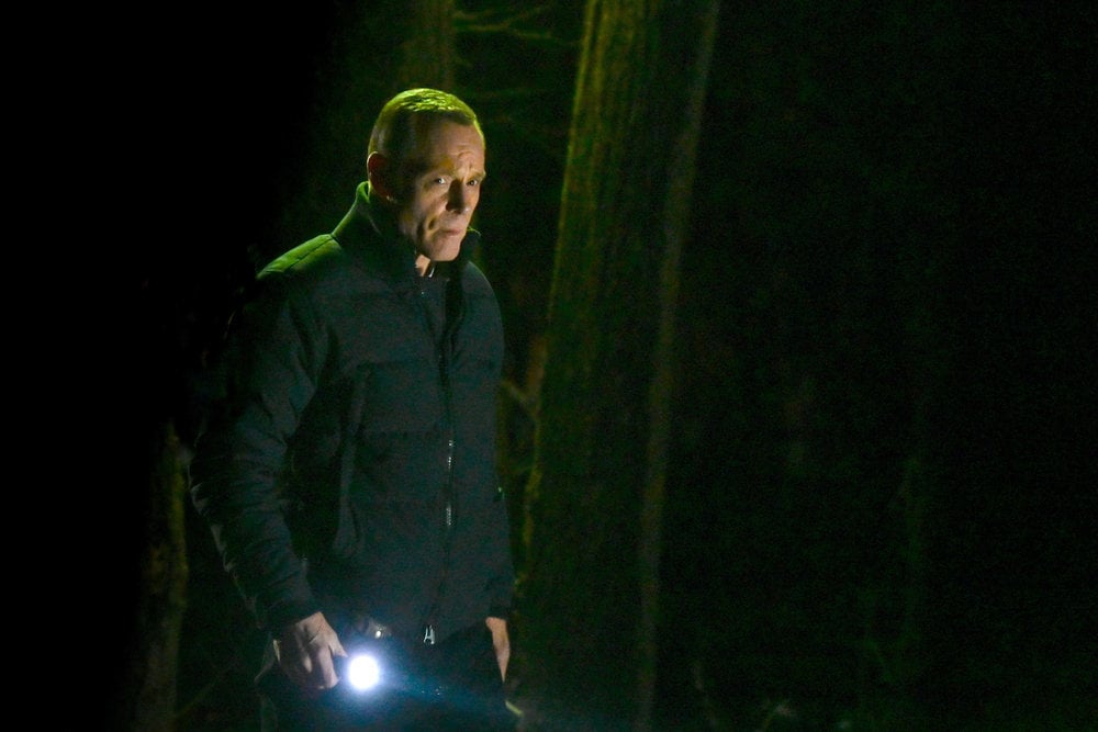 Chicago P.D. Season 11 Episode 7, Jason Beghe as Hank Voight walks through a wooded area at night with a flashlight looking concerned.