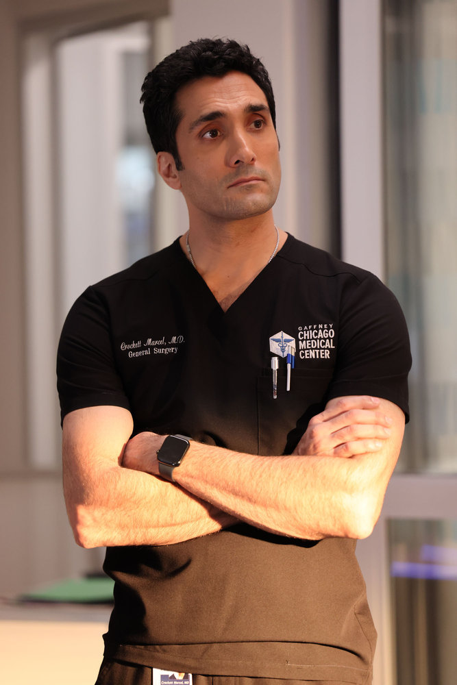 Chicago Med - Season 9 Episode 8 Dominic Rains as Dr. Crockett Marcel stands with a stern look on his face and his arms crossed.