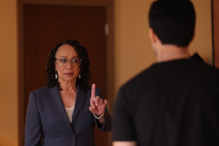 Chicago Med Season 9 Episode 7, S. Epatha Merkerson as Sharon Goodwin has a stern look on her face as she holds up one finger to Dominic Raines as Dr. Crockett Marcel, who's out of focus and his back is to the camera.