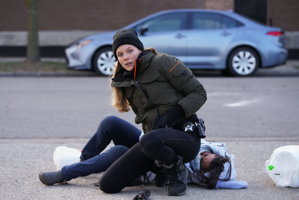 Chicago P.D. - Season 11 Episode 8 Tracy Spiridakos as Hailey Upton squats down by someone who is lying on the ground. Upton looks off toward something out of frame