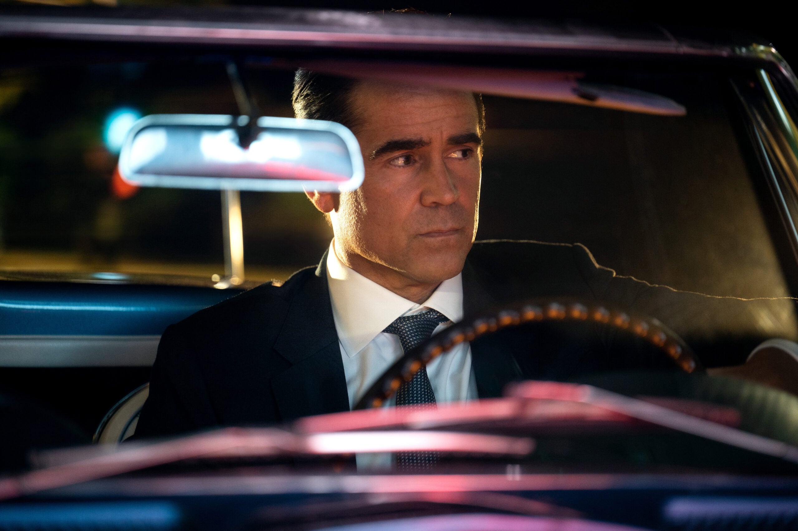 Still from Sugar Season 1 Episode 2 of Colin Farrell wearing a black suit and tie sitting behind the steering wheel of a car at night.
