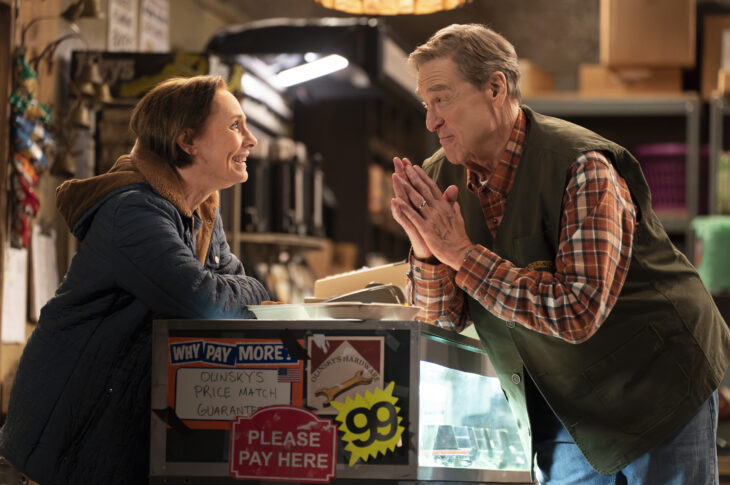 The Conners Season 6 Episode 7: LAURIE METCALF smiles at JOHN GOODMAN over the counter at the hardware store while JOHN GOODMAN has his hands together in a pleading nature.