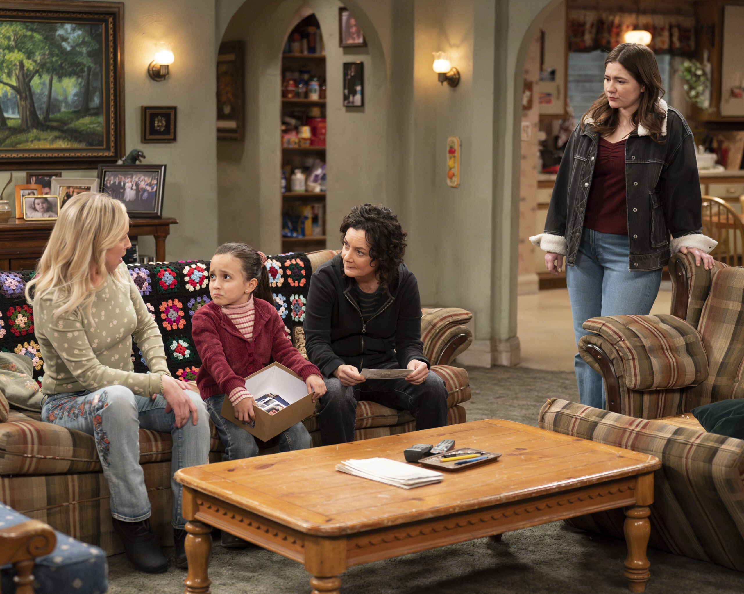 The Conners Season 6 Episode 7: LECY GORANSON, CHARLOTTE SANCHEZ, SARA GILBERT, EMMA KENNEY all hang out in the Conner living room talking about family members who have passed on while looking at pictures.