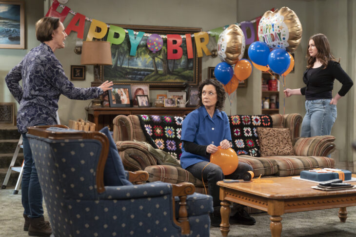 The Conners Season 6 Episode 8 - LAURIE METCALF, SARA GILBERT, EMMA KENNEY sit around the Conner living room with a Happy Birthday banner behind them.