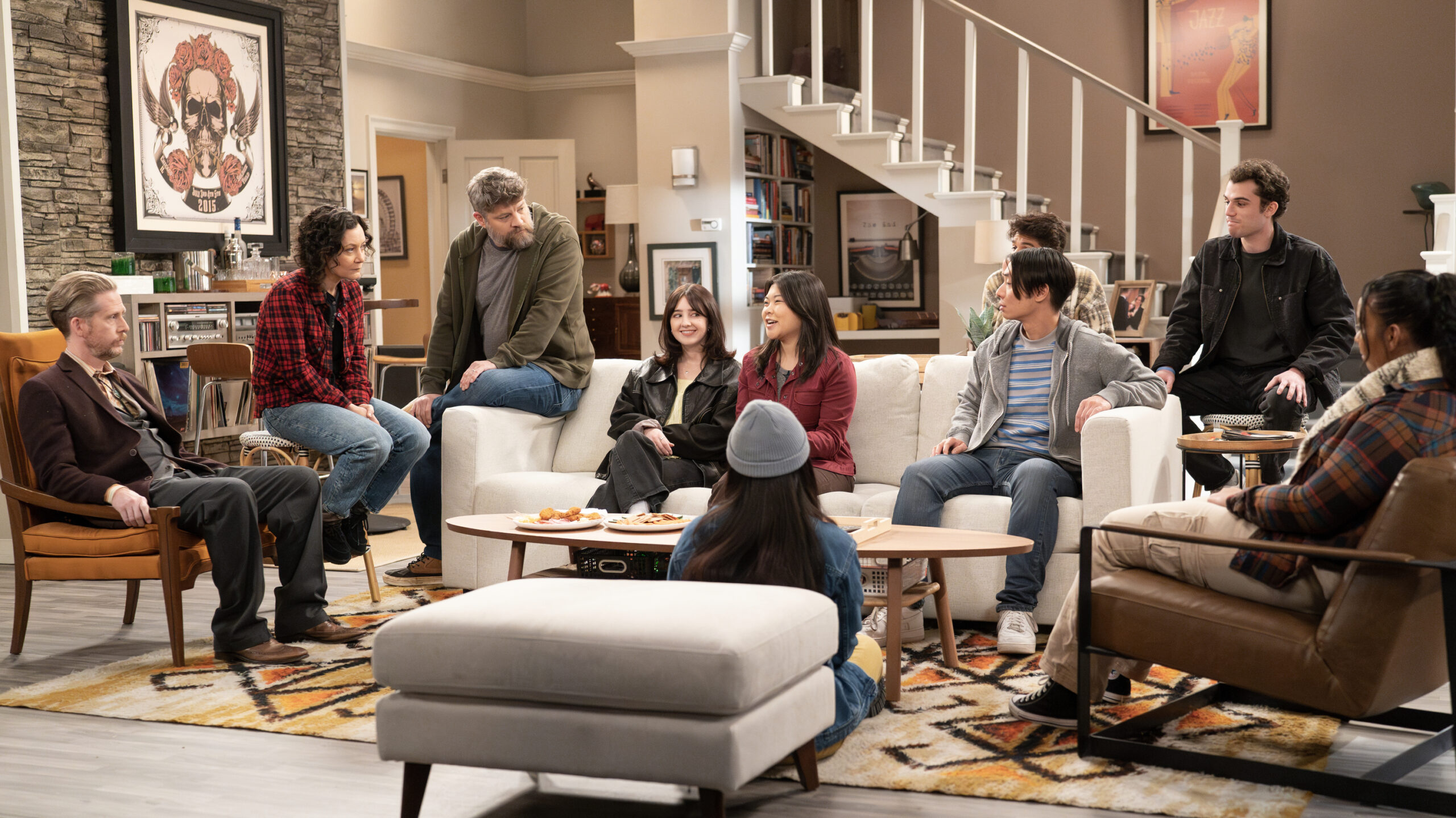 The Conners Season 6 Episode 8 - COLLIN CHRISTOPHER, SARA GILBERT, JAY R. FERGUSON, KIANA FONG all sit around Darlene and Ben's living room talking.