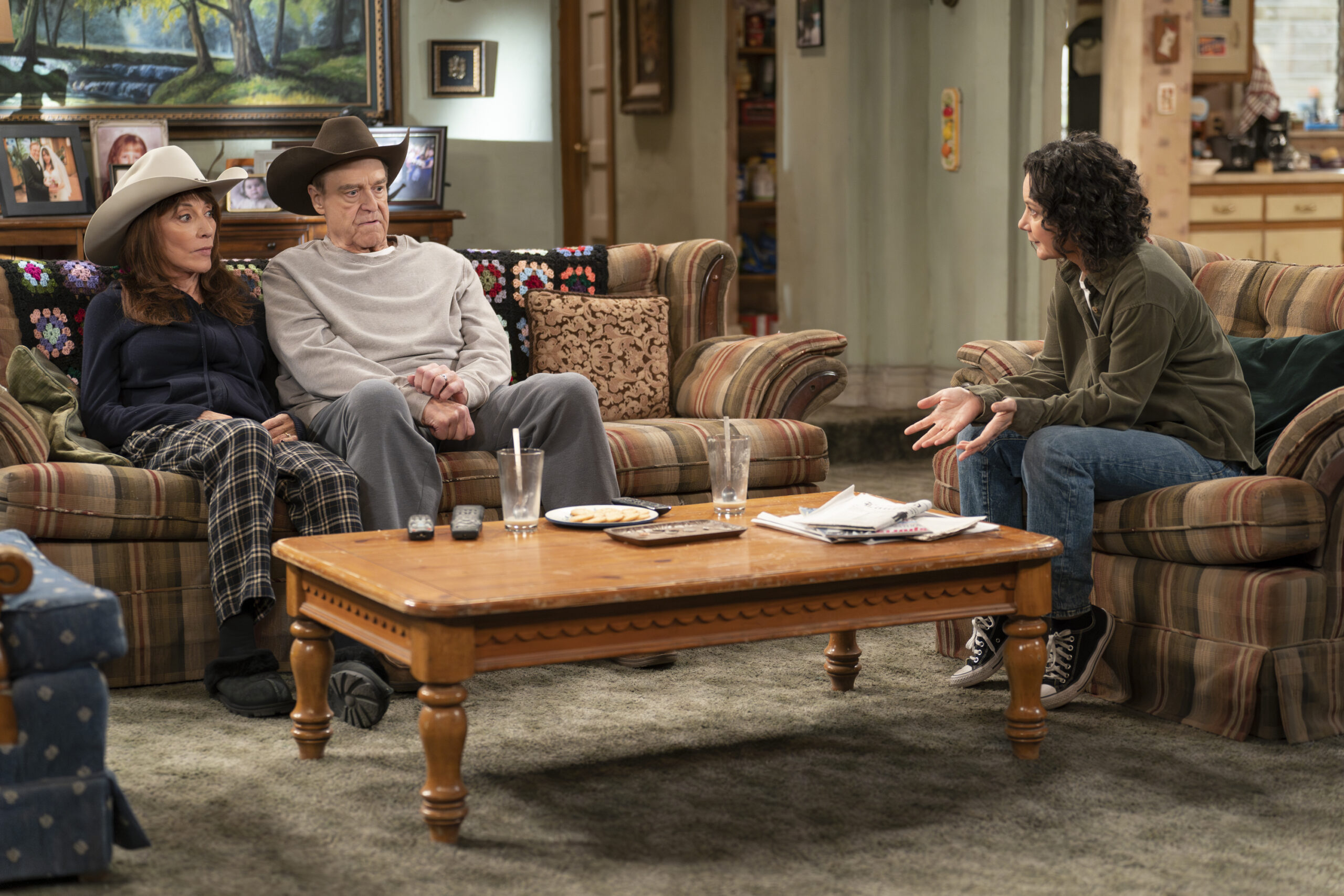 KATEY SAGAL, JOHN GOODMAN, SARA GILBERT | Tell-Tale TV The Conners Season 6 Episode 9 - KATEY SAGAL and JOHN GOODMAN sit on the couch while SARA GILBERT sits on the chair and chastises them.