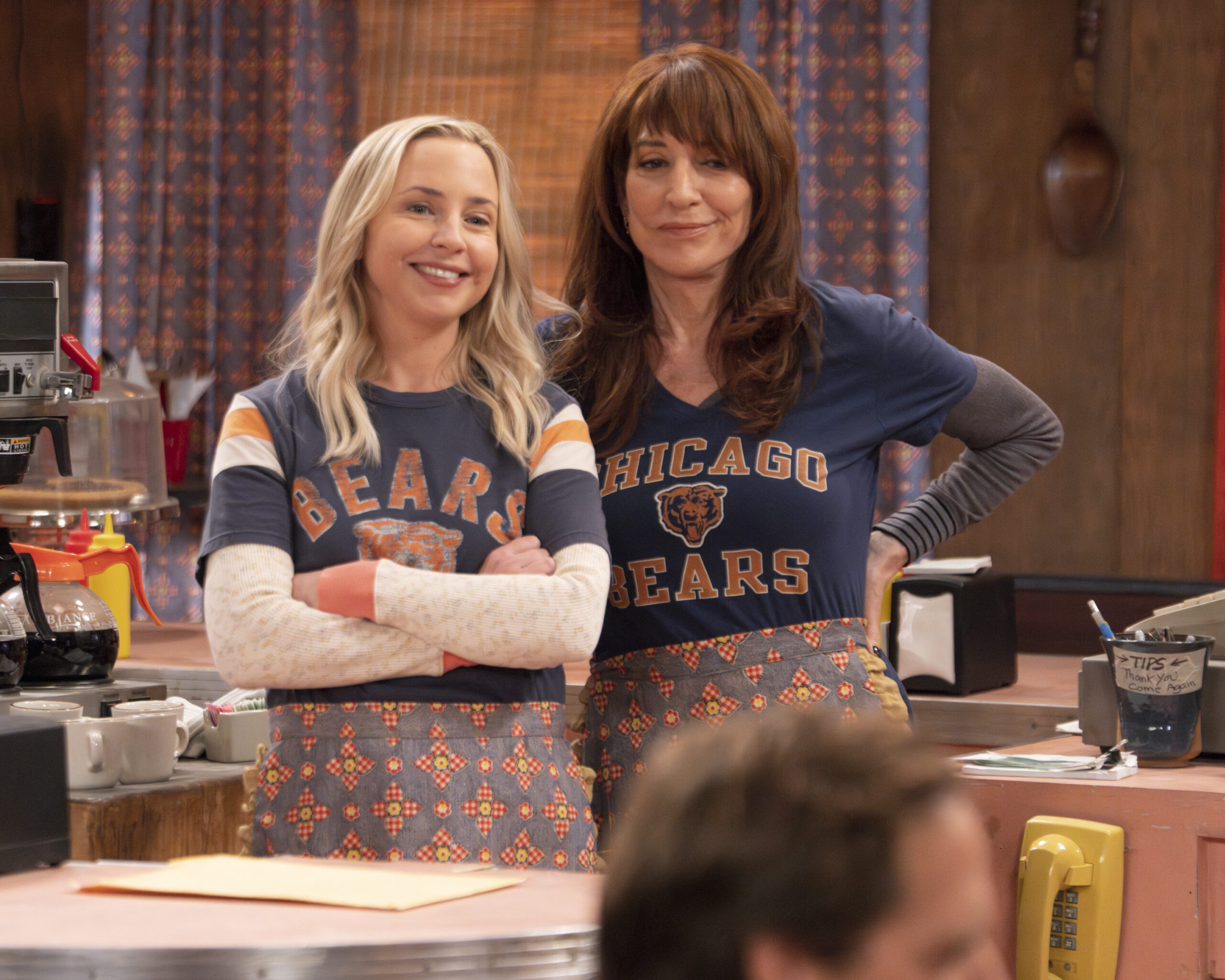 LECY GORANSON, KATEY SAGAL | Tell-Tale TV The Conners Season 6 Episode 10 - LECY GORANSON and KATEY SAGAL look on with a smile during Jackie's retirement party.