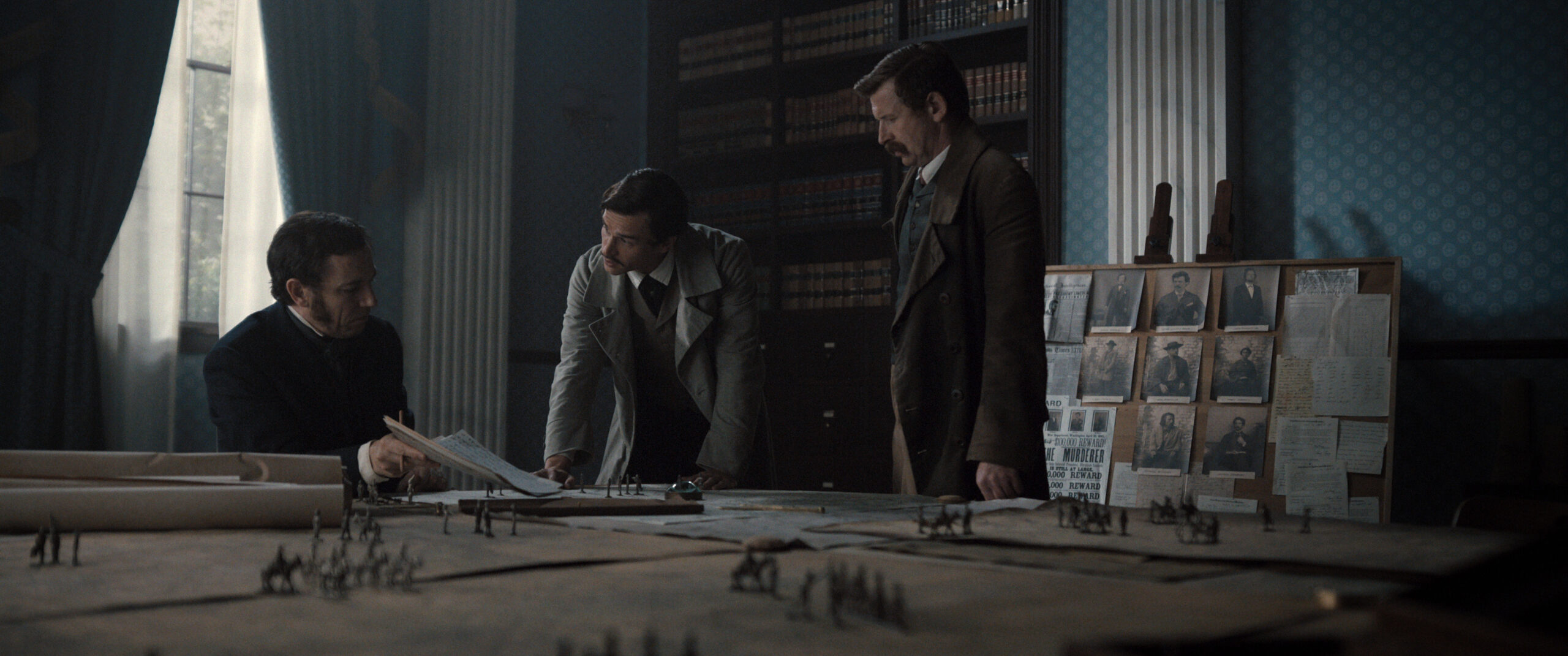 Still from Manhunt Season 1 Episode 5 of Tobias Menzies, Brandon Flynn and Damian O’Hare pictured from left to right at a table with papers and soldier figures on it.