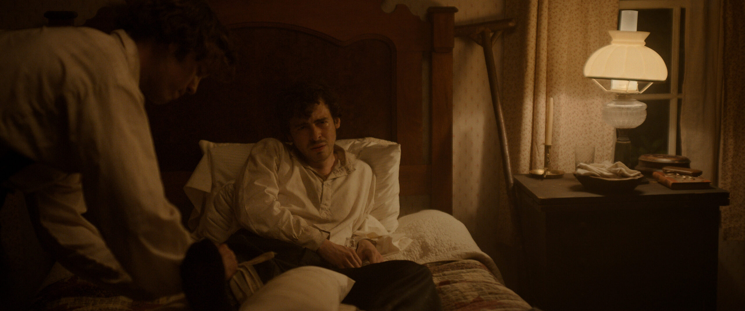 Still from Manhunt Season 1 Episode 6 of Anthony Boyle as John Wilkes Booth laying upright in a bed.