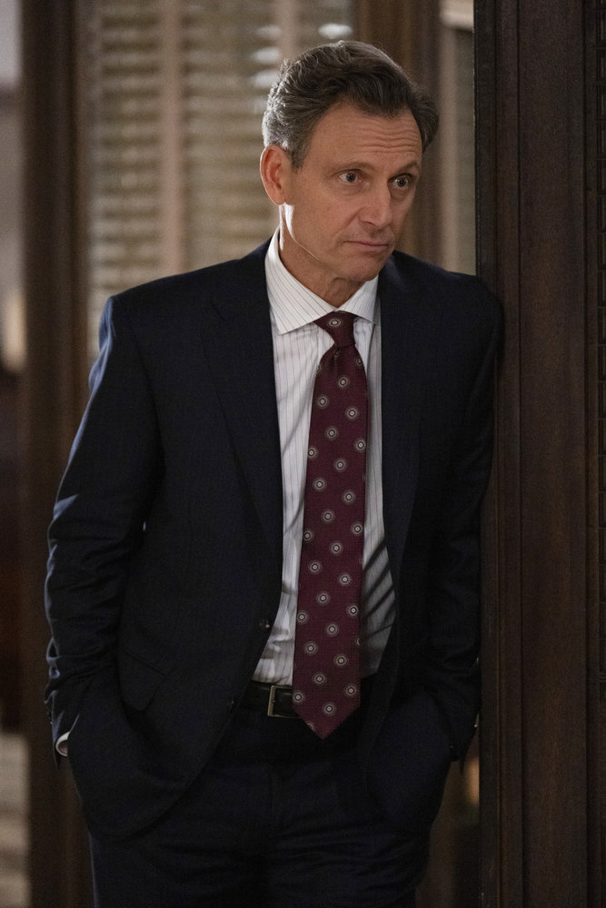 Law & Order Season 23 Episode 9 - Tony Goldwyn as DA Nicholas Baxter leans against a door frame with a serious look on his face.