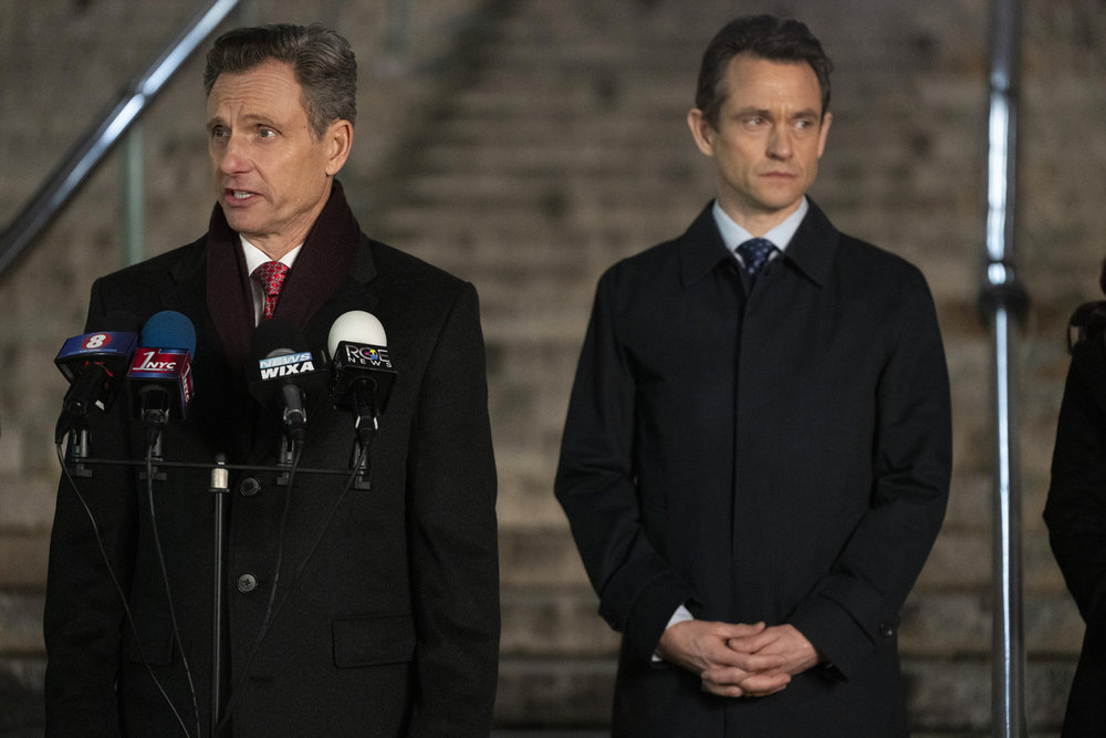 Law & Order - Season 23 | Tell-Tale TV Law & Order Season 23 Episode 10 - Tony Goldwyn as DA Nicholas Baxter stands next to Hugh Dancy as ADA Nolan Price on the steps of the courthouse behind some microphones speaking to the press.