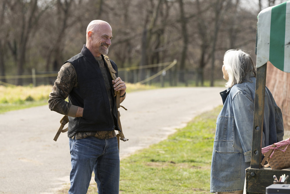 Law & Order: Organized Crime Season 4 Episode 9 - Christopher Meloni as Det. Elliot Stabler stands and smiles as he talks with Lois Smith as Mama Boone at a roadside stand.