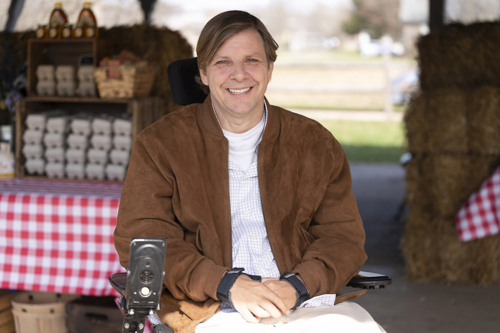 Law & Order: Organized Crime Season 4 Episode 9 - Tobias Forrest as Darian Morse, a wheelchair user, at a farm stand selling eggs with a smile on his face.