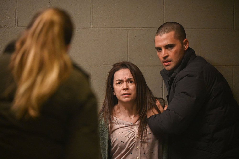 Chicago P.D. Season 11 Episode 10 - Tracy Spiridakos as Hailey Upton with her back to the camera interrogates Vanessa Martinez as Sonia Zamora while the woman is being held by Benjamin Levy Aguilar as Dante Torres.