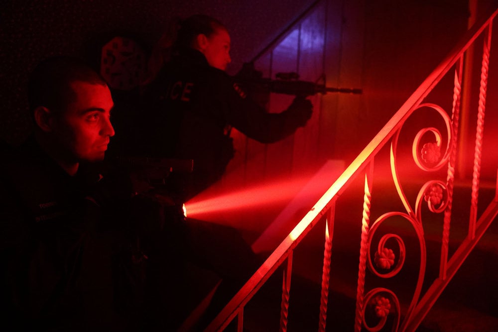 Chicago P.D. Season 11 Episode 10 - Benjamin Levy Aguilar as Dante Torres and Tracy Spiridakos as Hailey Upton approach a door by climbing some stairs with their guns raised.