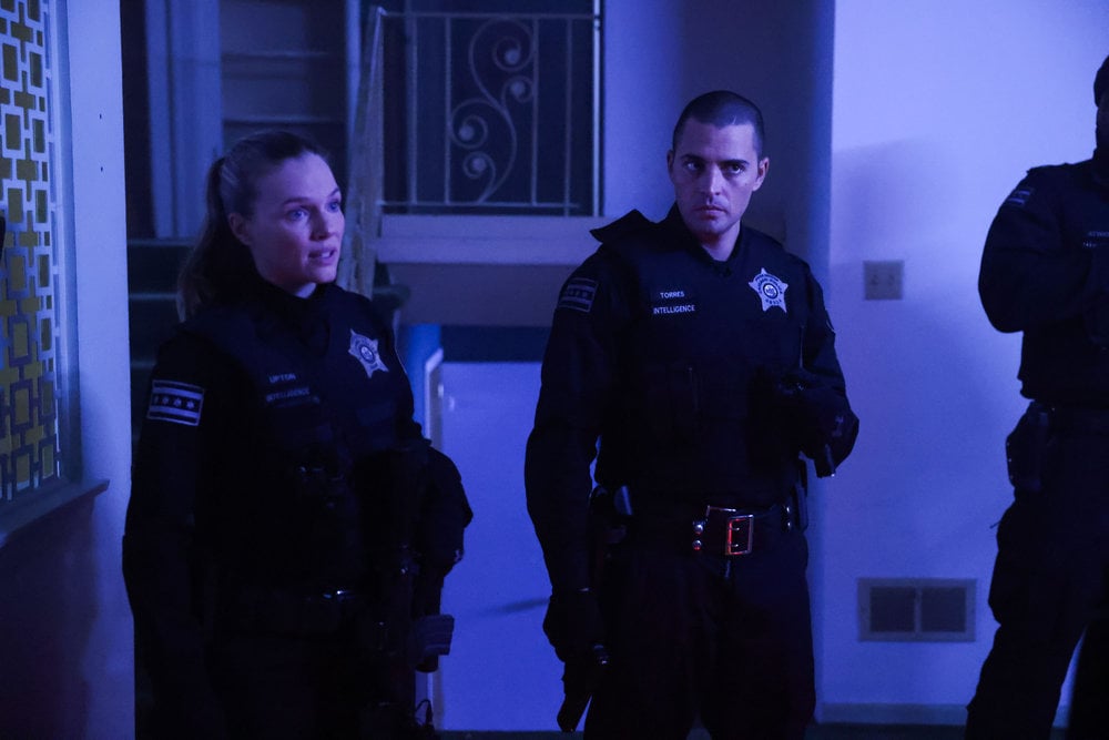 Chicago P.D. Season 11 Episode 10 - Tracy Spiridakos as Hailey Upton stands next to Benjamin Levy Aguilar as Dante Torres listening to someone out of frame.