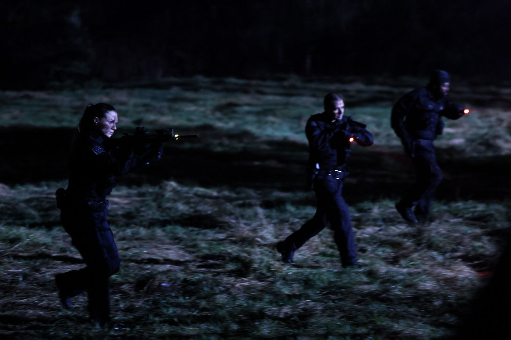 Chicago P.D. Season 11 Episode 10 - Tracy Spiridakos as Hailey Upton, Benjamin Levy Aguilar as Dante Torres, and LaRoyce Hawkins as Kevin Atwater approach a location in a line formation with their guns and flashlights drawn.