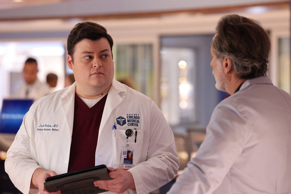 Chicago Med - Season 9 | Tell-Tale TV Chicago Med Season 9 Episode 10 - Conor Perkins as Dr. Zach Hudgins holds a tablet and looks skeptically at Steven Weber as Dr. Dean Archer who has his back to the camera.