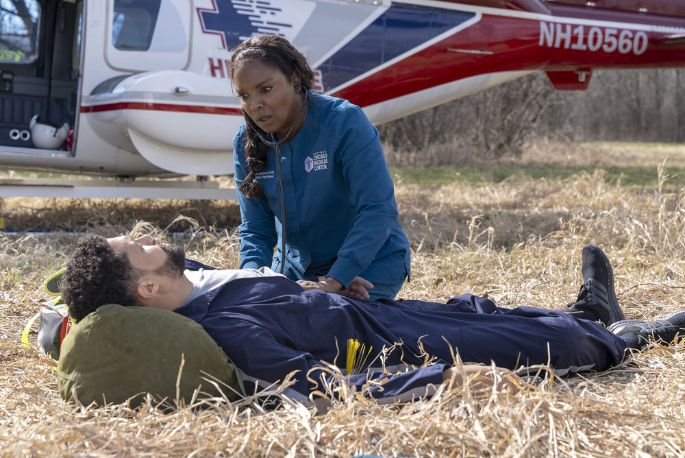 Chicago Med Season 9 Episode 10 - Henderson Wade as Dr. Loren Johnson lays on the ground with a medical emergency as Marlyne Barrett as Maggie Lockwood tends to his care.