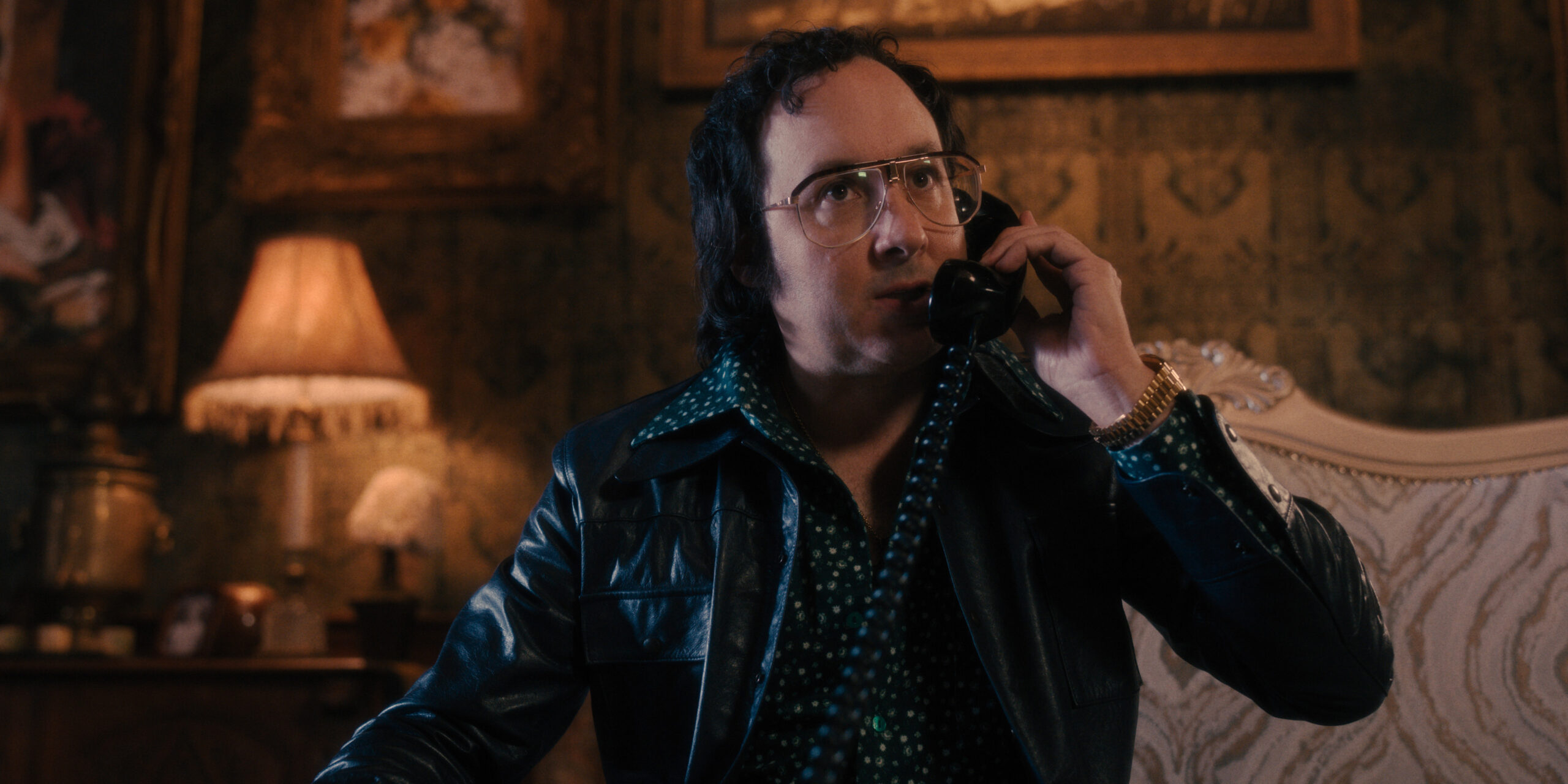 The Big Cigar Season 1 Episode 3 - P. J. Byrne | Tell-Tale TV Still from The Big Cigar Season 1 Episode 3 of P. J. Byrne wearing a polka dot shirt and leather jacket talking on the phone.