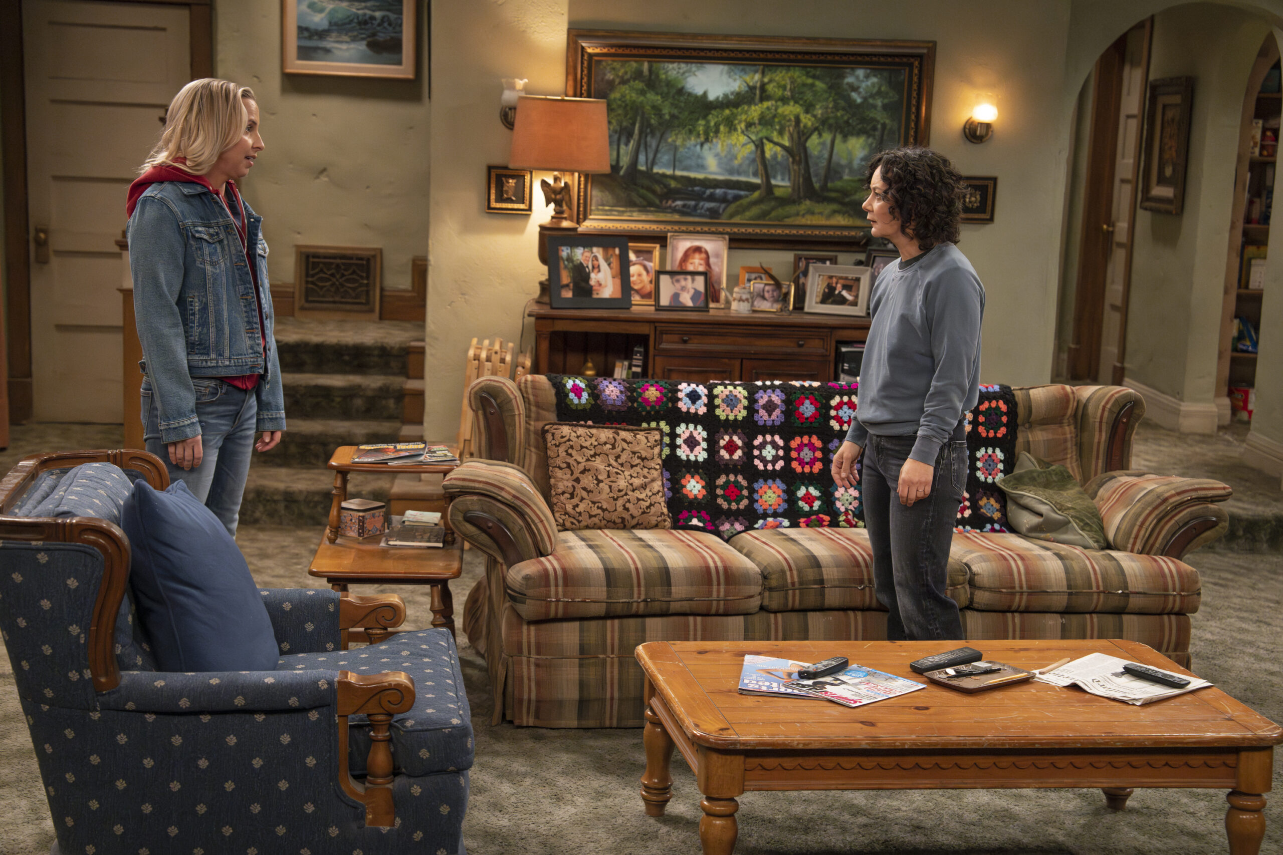 LECY GORANSON, SARA GILBERT | Tell-Tale TV The Conners Season 6 Episode 13 - LECY GORANSON and SARA GILBERT have a discussion standing in the Conner family living room.