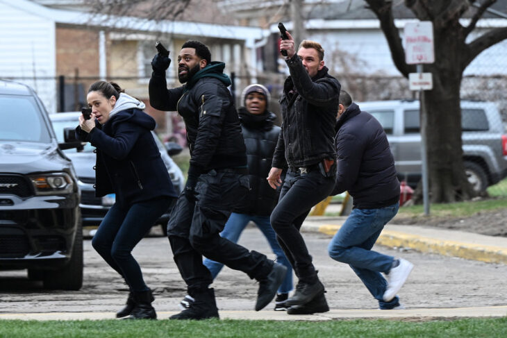 Chicago P.D. Season 11 Episode 12 - Marina Squerciati as Kim Burgess, LaRoyce Hawkins as Kevin Atwater, and Patrick John Flueger as Adam Ruzek walk with their guns drawn as they apprehend a suspect.