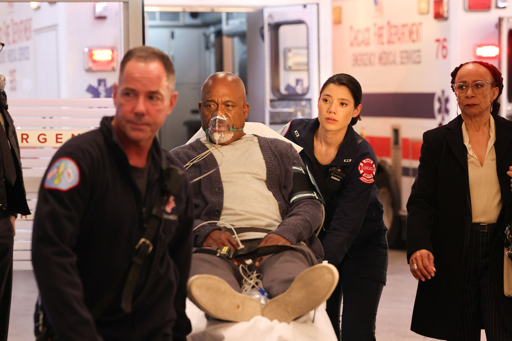 Chicago Med Season 9 Episode 12 - GregAlan Williams as Bert Goodwin comes into the ED on a stretcher with Hanako Greensmith as Violet Mikami and S. Epatha Merkerson as Sharon Goodwin.