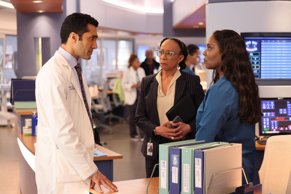 Chicago Med Season 9 Episode 12 - Dominic Rains as Dr. Crockett Marcel, S. Epatha Merkerson as Sharon Goodwin, and Marlyne Barrett as Maggie Lockwood stand together having a serious discussion.