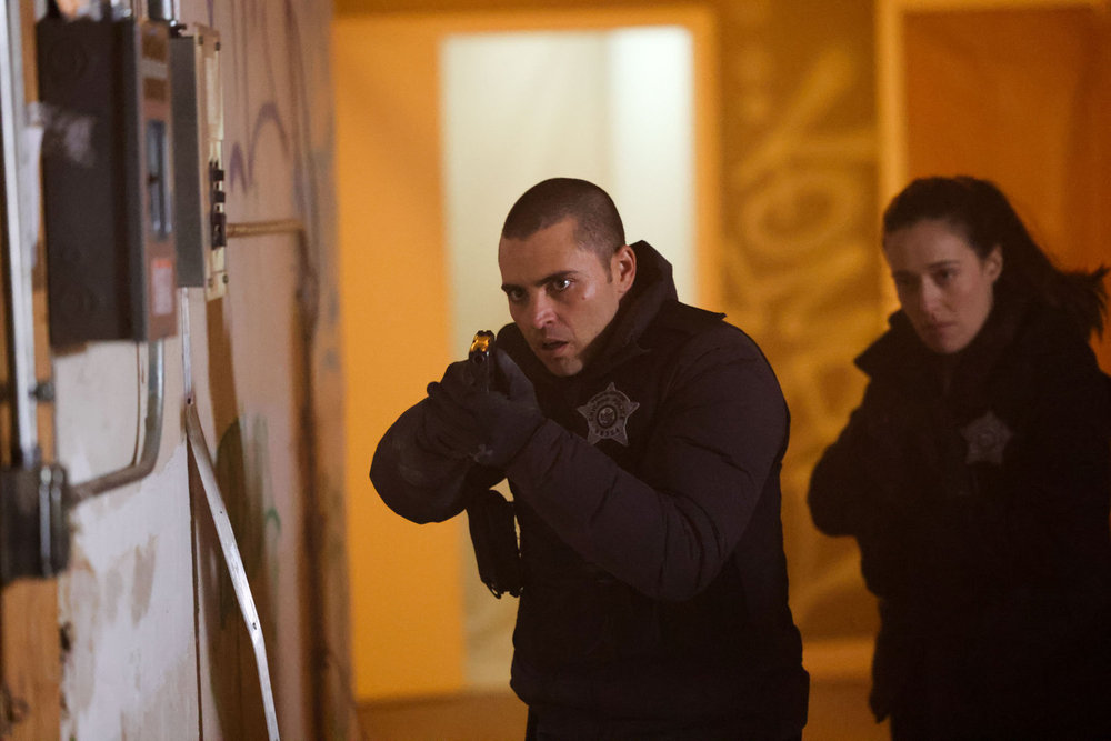 Chicago P.D. - Season 11 | Tell-Tale TV Chicago P.D. Season 11 Episode 13 - Benjamin Levy Aguilar as Dante Torres and Marina Squerciati as Kim Burgess walk through a building with their guns at the ready.
