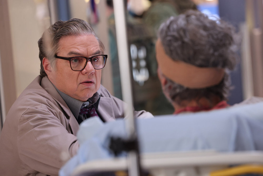 Chicago Med Season 9 Episode 13 - Oliver Platt as Dr. Daniel Charles sits with a patient and talks to him.