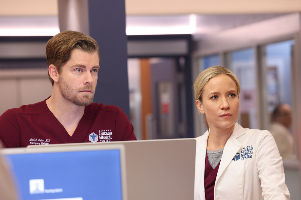Chicago Med - Season 9 | Tell-Tale TV Chicago Med Season 9 Episode 13 - Luke Mitchell as Dr. Mitch Ripley and Jessy Schram as Dr. Hannah Asher stand at the computer and observe something out of frame.