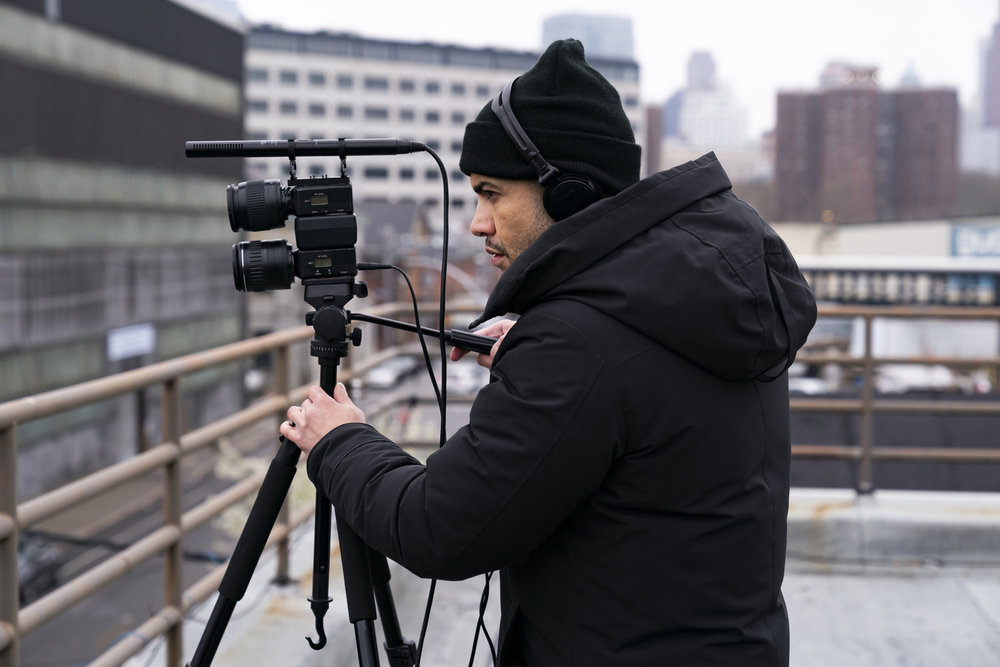 Law & Order: Organized Crime - Season 4 | Tell-Tale TV Law & Order: Organized Crime Season 4 Episode 12 - Rick Gonzalez as Det. Bobby Reyes stands on a roof with a camera.