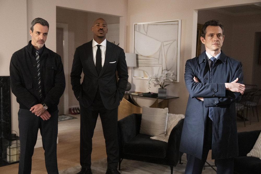 Law & Order - Season 23 | Tell-Tale TV Law & Order Season 23 Episode 12 - Reid Scott as Det. Vincent Riley, Mehcad Brooks as Det. Jalen Shaw, and Hugh Dancy as Assistant District Attorney Nolan Price stand in a the living room of a witnesses home.
