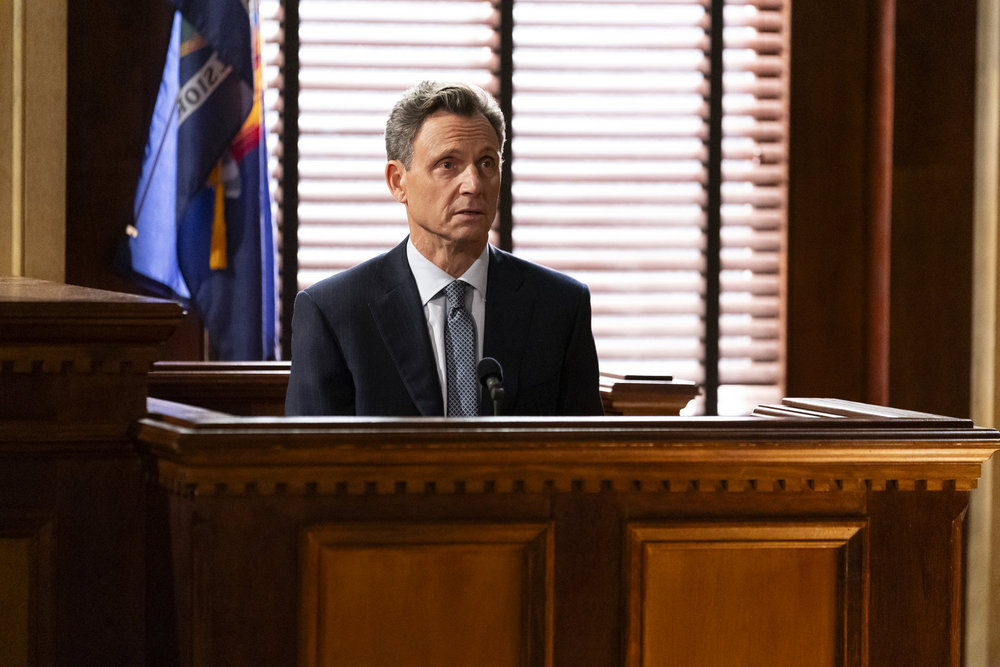 Law & Order Season 23 Episode 13 - Tony Goldwyn as DA Nicholas Baxter sits on the stand in court.