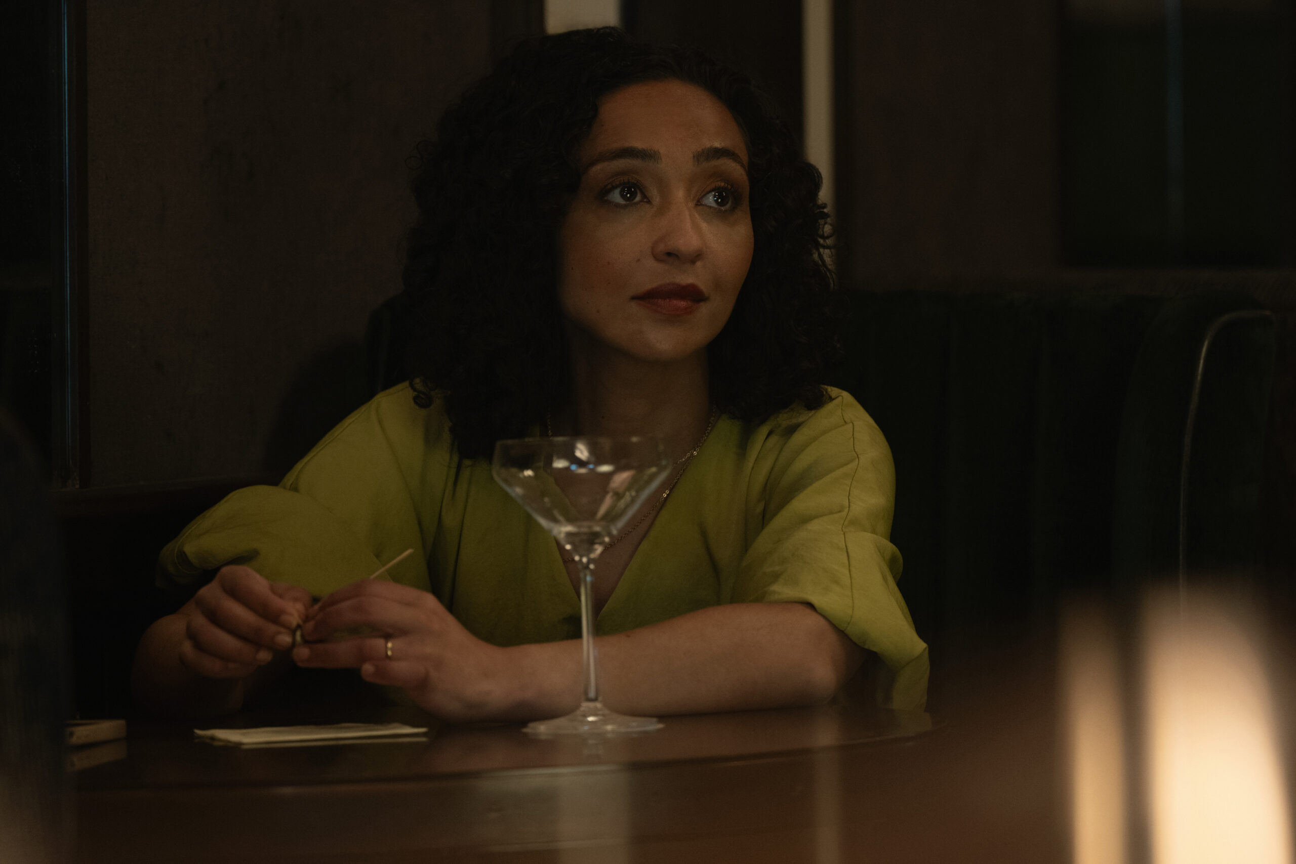 Ruth Negga sitting at a bar in front of a martini glass.
